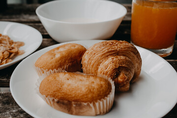 Delicious breakfast with croissant, muffin, cereals and orange juice served on a wooden table.