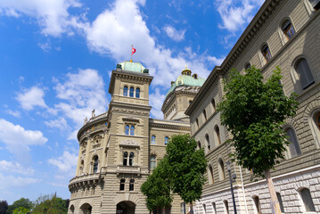 Federal Palace of Switzerland with waving Swiss flags at City of Bern, capital of Switzerland, on a blue cloudy summer day. Photo taken June 16th, 2022, Bern, Switzerland.