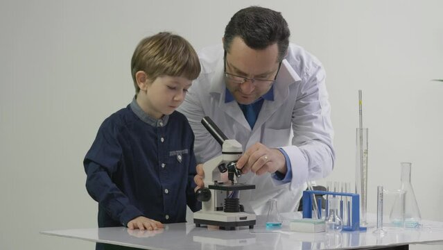 Teacher learning the little student to use chemical laboratory microscope