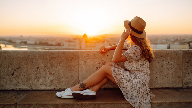 Young female tourist enjoys the view of the city at sunset. back view.  Lifestyle, travel, tourism, nature, active life.