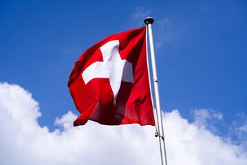 Swiss flag waving at local mountain Gurten, Canton Bern, on a sunny summer day with blue cloudy background. Photo taken June 16th, 2022, Gurten, Switzerland.