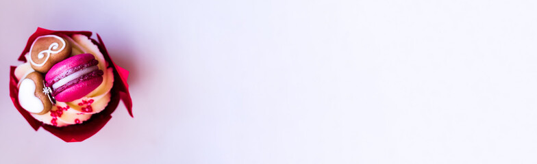 Appetizing red cupcake with a diamond ring inside for a marriage proposal on a light background. Banner with place for text. Sweet holiday dessert with cream, gingerbread and macaroons.