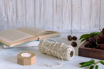 Fototapeta na wymiar Cozy summer composition with ripe cherries, candles and books on white wooden background. 