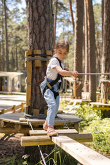 Kid climbing in rope course in adventure park. Children in forest rope park.