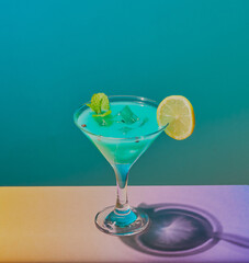 Blue cocktail on a blue background, with a purple and yellow gradient surface.