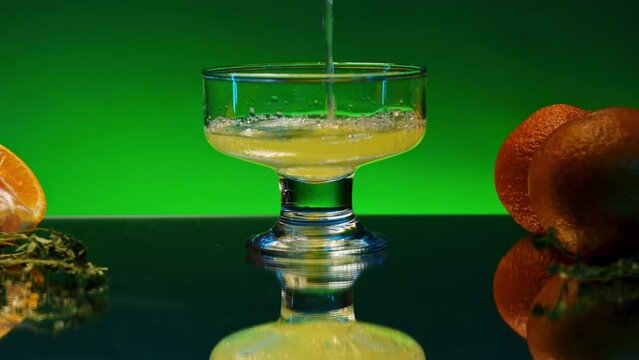 Close up of pouring orange soda into the glass. Stock clop. Soft drink with the taste of citrus and orange fruits on the reflective table surface.