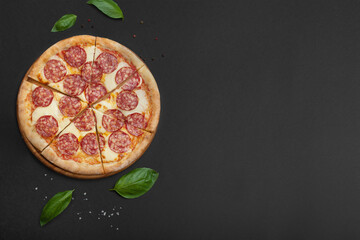 Pepperoni pizza with basil and spices on a black background