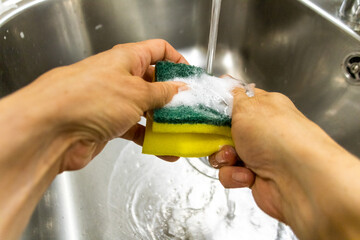 person with scourer and soap washing in kitchen sink
