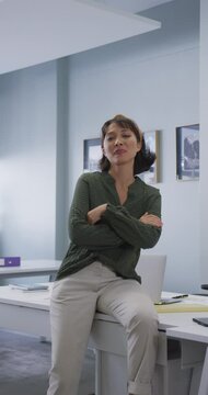 Vertical video of portrait of happy asian businesswoman looking at camera at office
