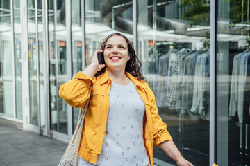 Happy confident smiling plus size curvy young woman with shopping bags walking on city street near shop windows