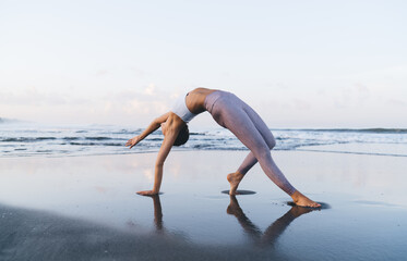 Caucasian female in tracksuit enjoying free time for training body vitality and flexibility during morning at coastline beach,slim woman stretching muscles during yoga practice for exercising in asana