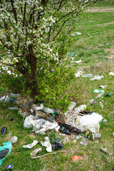 A pile of garbage in a clearing in the countryside against the backdrop of a flowering tree on a spring day. Vertically.