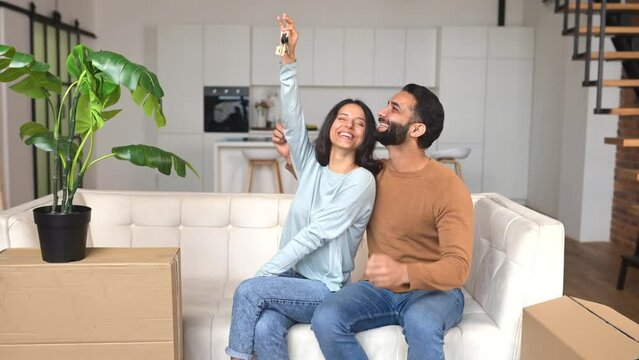 Excited proud overjoyed Indian couple showing keys from new home, rejoicing in euphoria to goal achievement, celebrating buying of own real estate, raising hands up and screaming,ethnic couple move in