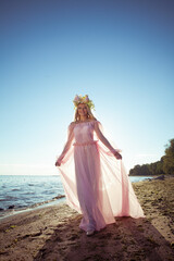 Summer woman portrait in long dress on sea coast against sun