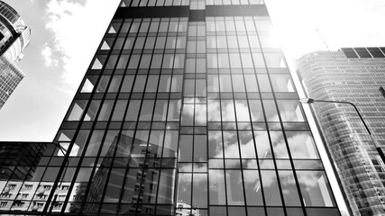 Fototapeta premium Modern office building with glass facade on a clear sky background. Transparent glass wall of office building. Bright sunny day with sunbeams on the sky. Black and white.