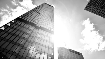 Modern office building with glass facade on a clear sky background. Transparent glass wall of office building. Bright sunny day with sunbeams on the sky.  Black and white.