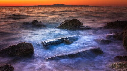 Widok skał oblewanych przez morze o wschodzie słońca przy kolorowym niebie - obrazy, fototapety, plakaty