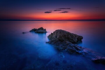 Fototapeta Widok skał oblewanych przez morze o wschodzie słońca przy kolorowym niebie obraz