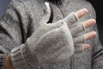 Hand of a man in a woolen glove with open fingers against the background of a blurred torso in a warm jacket.