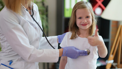 Doctor listens to child with stethoscope girl holds thumbs up