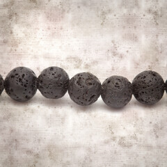 square stylish old textured paper background with necklace made of black volcanic lava beads