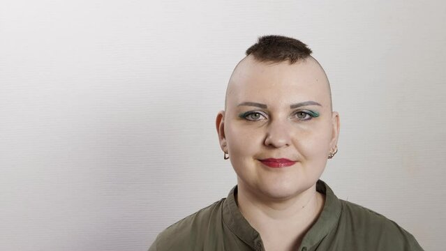 A shaven woman with a mohawk smiles showing class ok to the camera. Medium plan