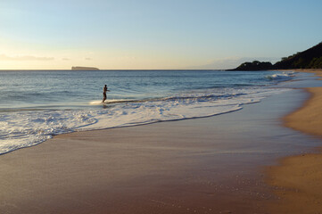 a man skimboarding with back to camera at sunset