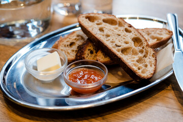 fresh bread on a metal plate with ramikins of butter and jam