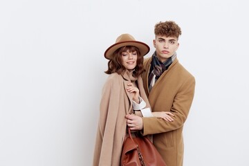a stylish, loving couple, a man and a woman are standing on a white background in an autumn coat, and a woman is clinging to a man with her hands folded on him