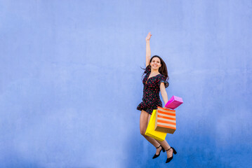 portrait of young beautiful woman jumping on colorful background wall holding shopping bags on...