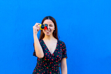 portrait of young woman taking a picture holding a retro vintage camera on colorful background wall in summer. happy and joyful caucasian girl smiling at camera making a photo. lifestyle concept