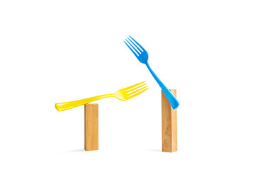 Dos tenedores celeste y amarillo apoyados sobre dos bases de madera sobre un fondo blanco liso y...