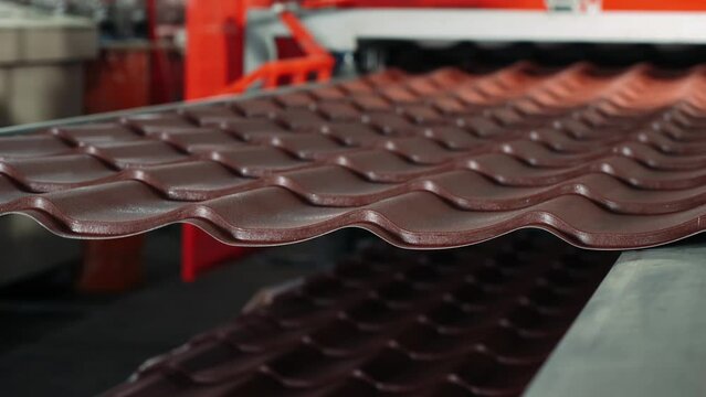 Production of brown metal roof tiles made from galvanized and painted steel on a sheet metal forming machine in a metal fabrication factory.