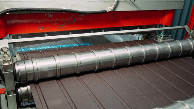 Production of brown metal roof tiles made from galvanized and painted steel on a sheet metal forming machine in a metal fabrication factory.