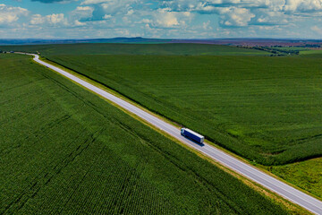 blue truck driving on asphalt road along the green fields. beautiful clouds in the blue sky. Aerial...