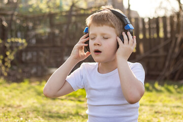 Close-up of teenager boy with headphones with closed eyes listening to music on a mobile tablet and relaxing in the fresh air in nature