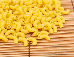 Closeup of dry elbow macaroni pasta and spoon on bamboo mat