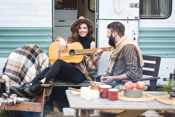 Young beautiful loving couple travelling across country in the van. Millennial man and woman in a travel camper. Cozy atmosphere, vacations vibe. Playing guitar, drinking tea, cooking on a campfire