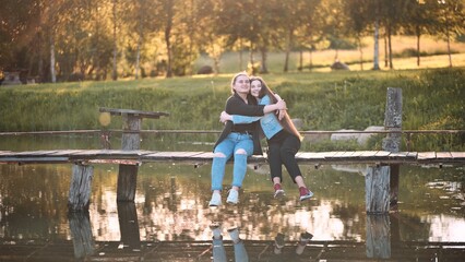 Two friends are sitting and hugging on the bridge by the river.