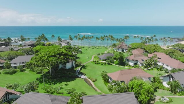 Cinematic aerial shot of famous Poipu village in Kauai, Hawaii island at summer sunny day. Aerial view of luxury beach with Polynesian village buildings surrounded by lavish greenery landscape, USA 4K