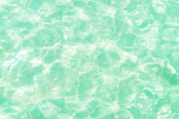 Defocused blurred clear green water. Sun glare and shadows in calm water. Trendy abstract nature texture background. Summer coolness. Copy space for text