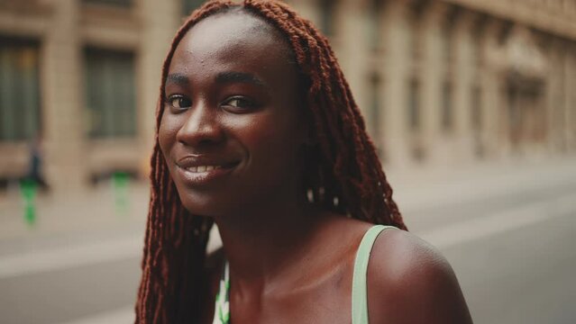 Close-up of beautiful woman with African braids turns his head and looks at the camera against the building background. Close-up Slow Motion