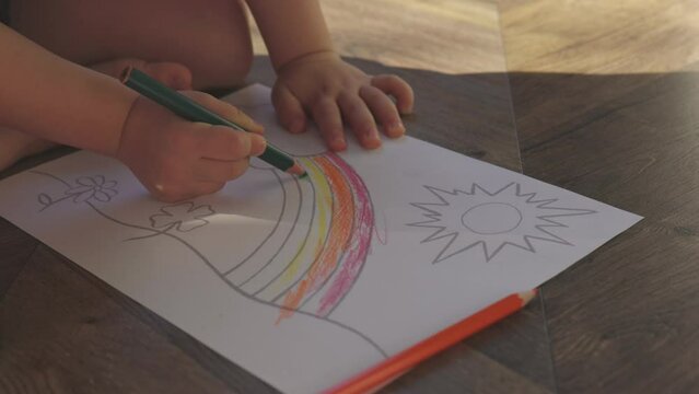 unrecognizable baby child hands coloring rainbow on white sheet paper, using colorful crayons or pencils. concept of art education, children learning developing skills. kid home indoor activity 