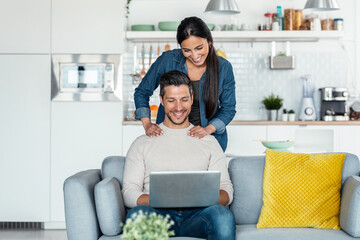 Happy beautiful couple using their laptop to searching voyage while sitting on the couch at home.