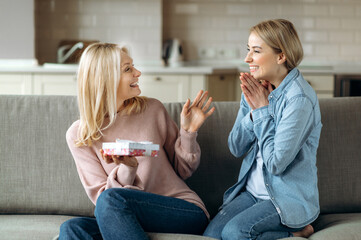 Surprise for mother's day or birthday. Loving young adult daughter giving a present to her beloved...
