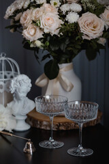 A creamy bouquet of roses and chrysanthemums, candles and glasses in the rays of light on a black table. The interior of the house is in the style of Provence. The concept of home comfort and decor.