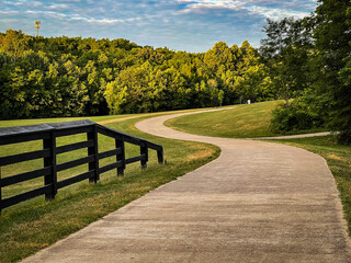 Fototapeta na wymiar Curves of a path forward in Veteran's park in Lexington, Kentucky. Wooden fence as a rail in the left side of the image 