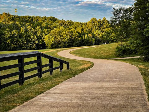 Curves of a path forward in Veteran's park in Lexington, Kentucky. Wooden fence as a rail in the left side of the image 