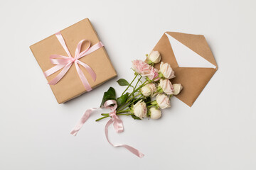 Envelope, gift box and rose flowers on white background, top view