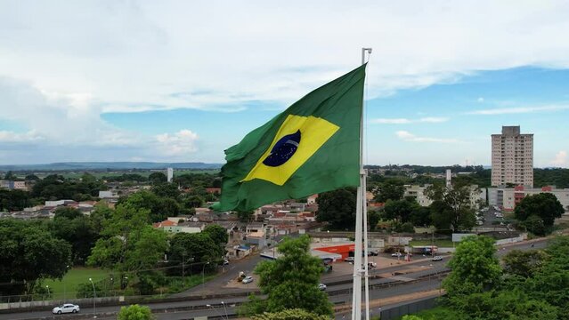 Brazilian flag flying in a city, next to busy streets and avenues with traffic